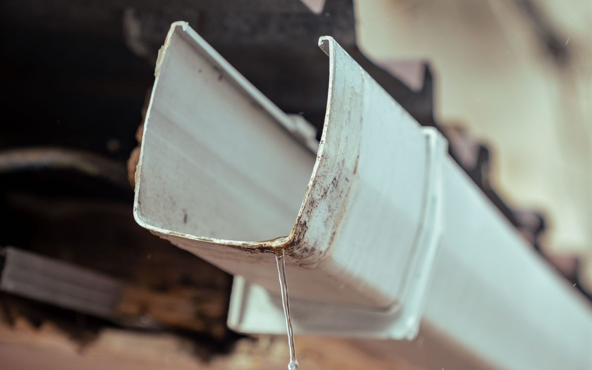 Rainwater running through a gutter with visible rust and fascia wear