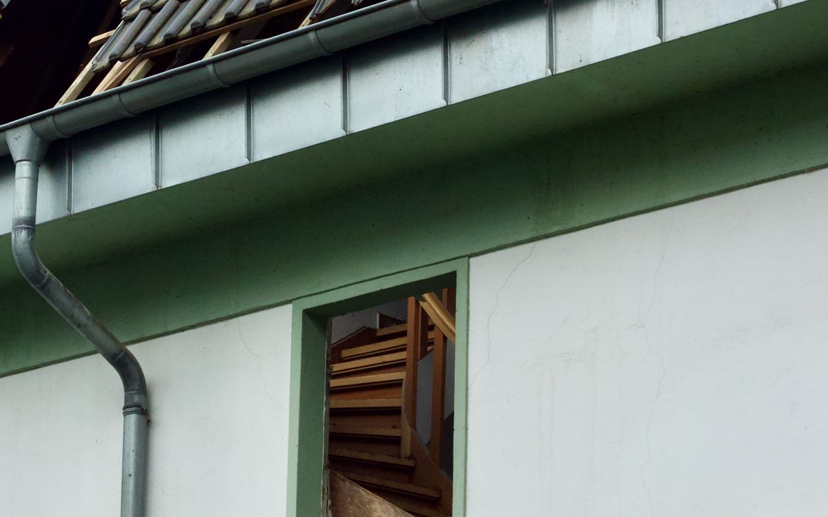 Storm damaged roof edge with displaced tiles, bent gutter and a broken window below