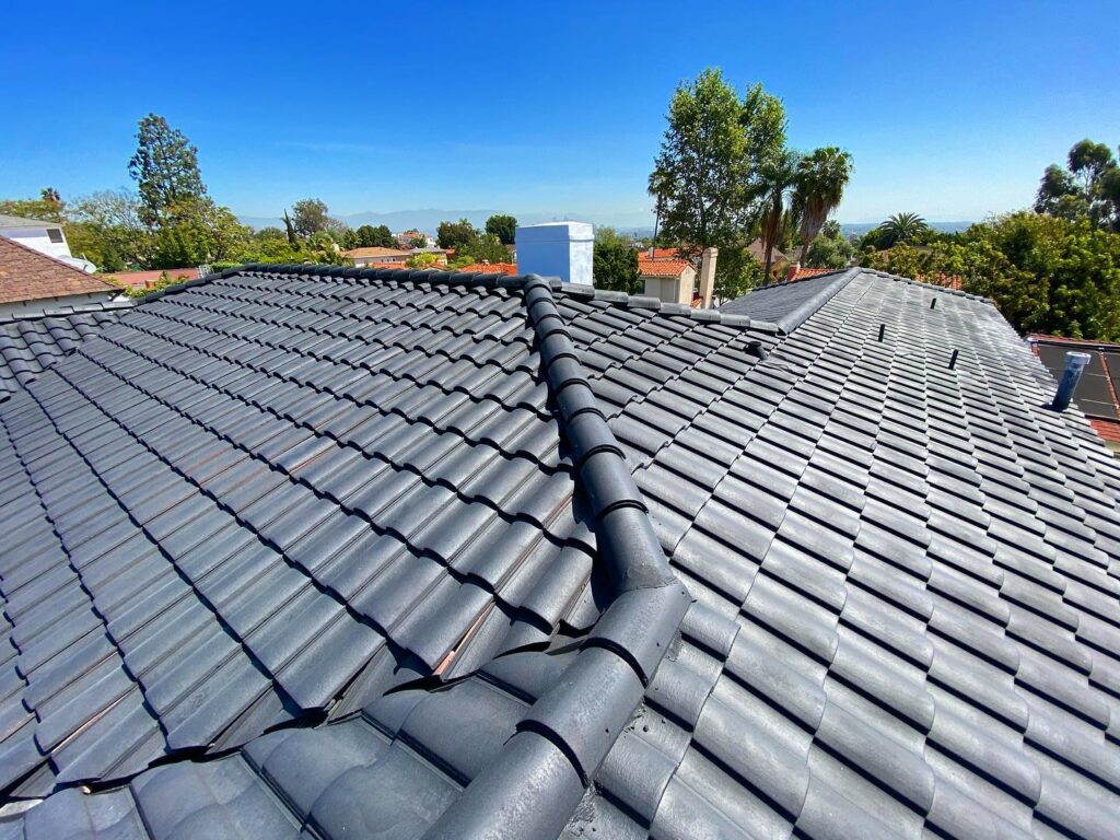 Modern gray tile roof under a clear blue sky, surrounded by lush greenery and residential buildings.
