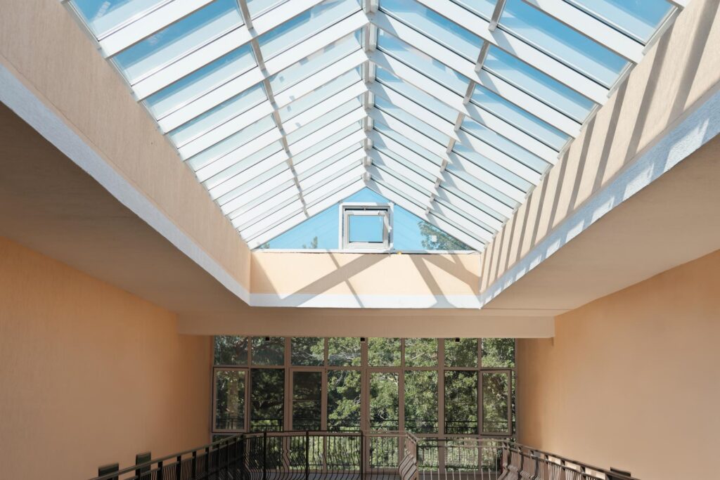 Interior view of a modern building featuring a large glass skylight that allows natural light to illuminate the space, with a balcony railing and large windows overlooking greenery.